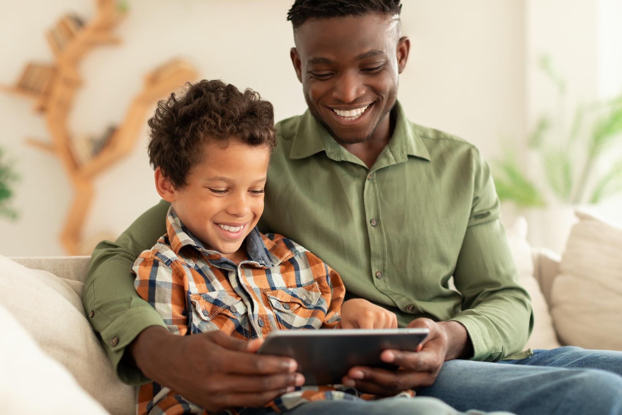 Happy Black Man And His Son Using Digital Tablet Indoors